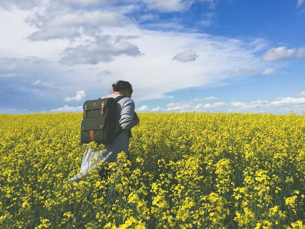 hispanohablantes Canadá chica morena de espaldas con una mochila andando por un prado